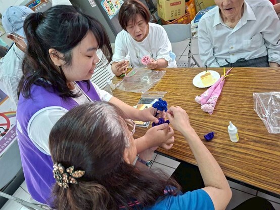高齡健康照護系（原高齡學程）衛可新校友（左紫背心）引導長輩製作康乃馨吊飾。圖片
