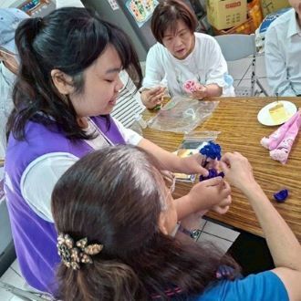 330高齡健康照護系（原高齡學程）衛可新校友（左紫背心）引導長輩製作康乃馨吊飾。